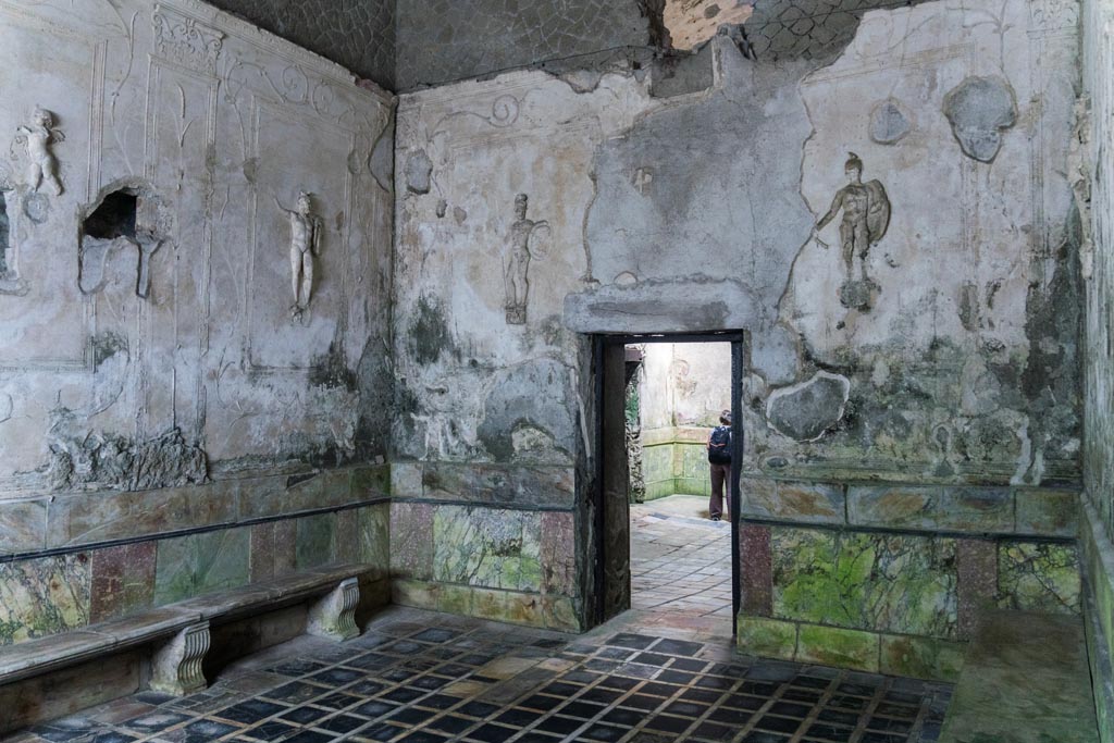 Herculaneum Suburban Baths. October 2023.
Tepidarium, north-west corner and north wall with doorway into frigidarium. Photo courtesy of Johannes Eber.
Decorative stucco warriors on white stucco panels were set into the walls of the tepidarium.
In this room were eight large white rectangular panels.
On seven of these panels were depicted stucco warriors (six showed warriors carrying spears, the seventh carrying a sword).
On the eighth panel were two stucco flying cupids carrying baskets of fruit and garlands.
